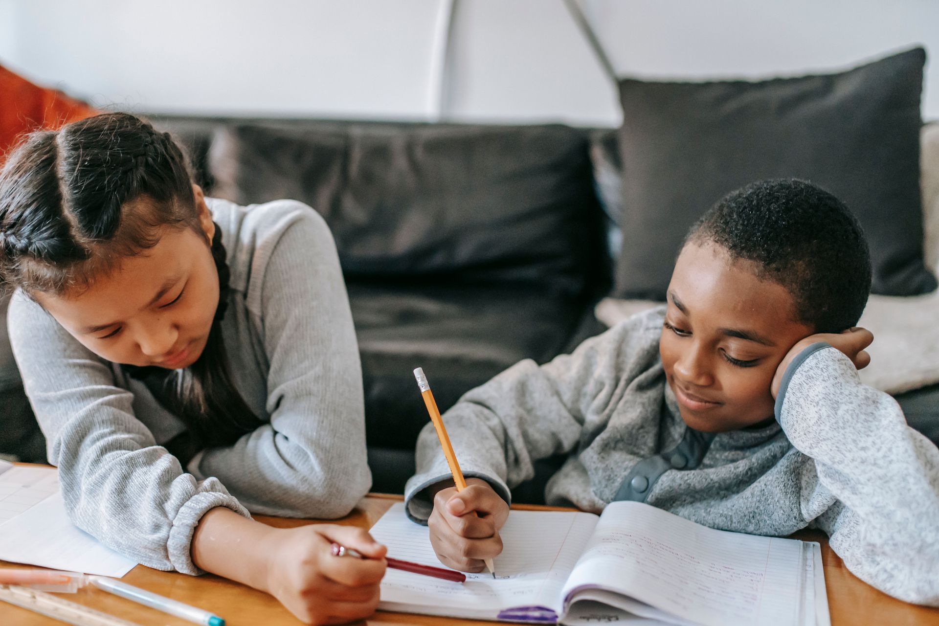 Crop diligent multiracial classmates with copybooks doing homework at table in house in daylight
